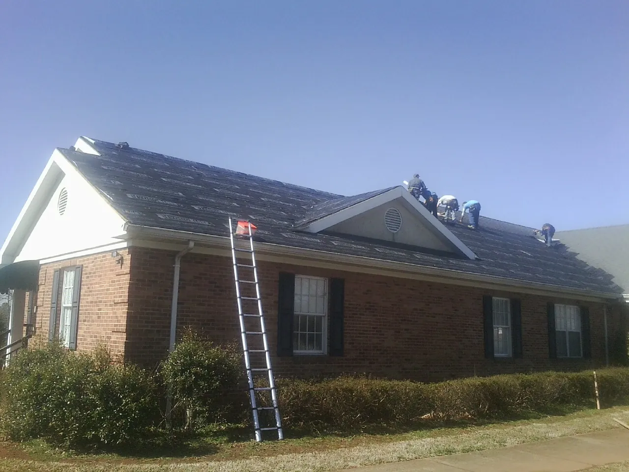 Crew tearing shingles off a brick ranch roof with a ladder set — Metal Roof Repair work by our crew in Middlebury
