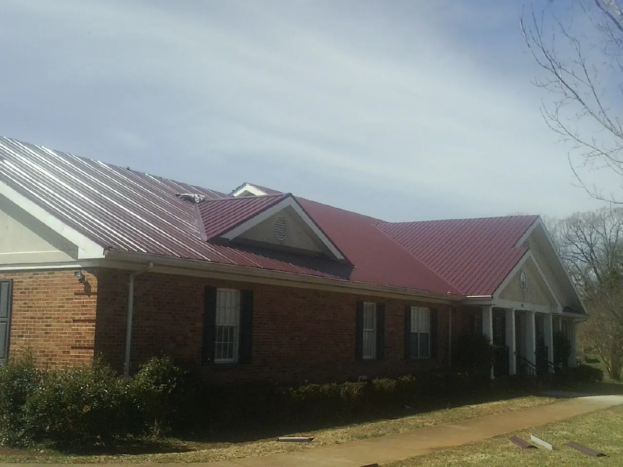 Red metal roof with gabled entries on a long brick building, from a Hail Damage Roof Repair job in Middlebury
