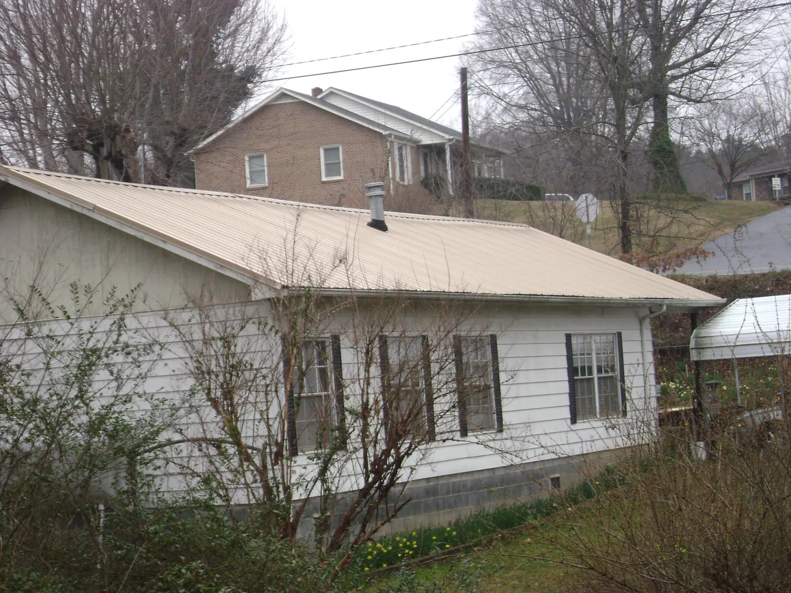 Tan metal roof on a white sided house set into a hillside — Commercial Roofing by Roofing Brothers in Middlebury